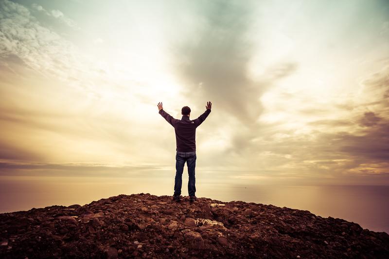 Man standing on hill raising hands to the sky