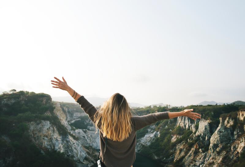 woman throwing her arms up in celebration looking out over cliff