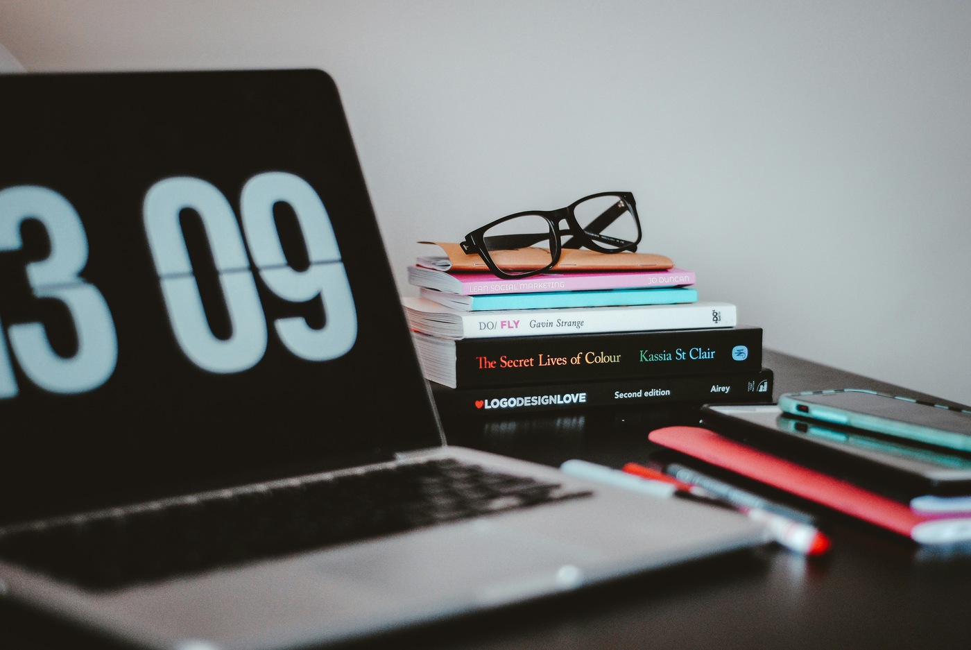 computer laptop next to books, pens and glasses indoors on desk