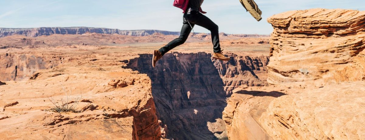 guy jumping over a chasm outdoors in desert