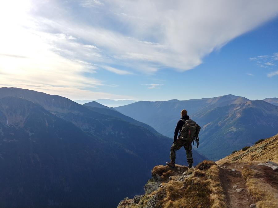 adventure: man standing on the edge of a cliff looking out at the mountains