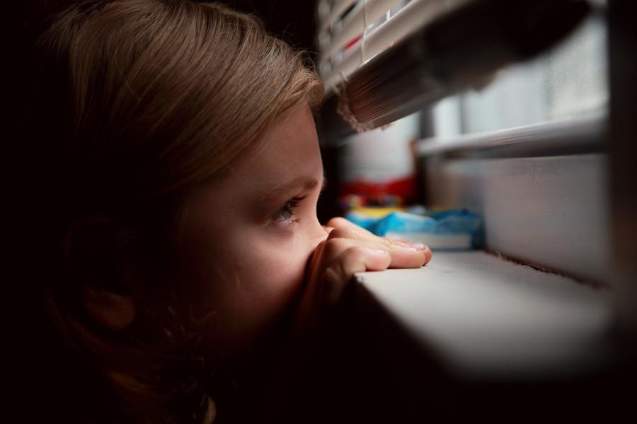 girl looking through the blinds on a window