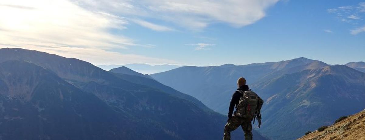 adventure: man standing on the edge of a cliff looking out at the mountains