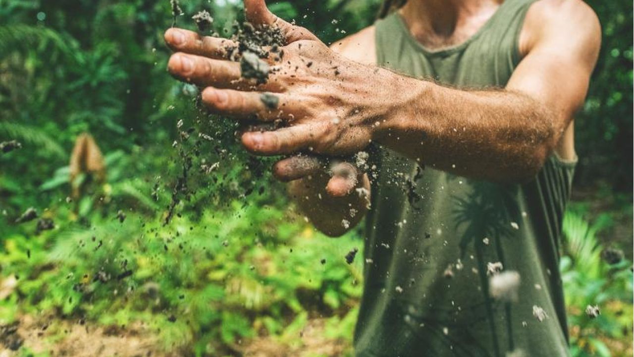 man rubbing dirt together in hands in forest