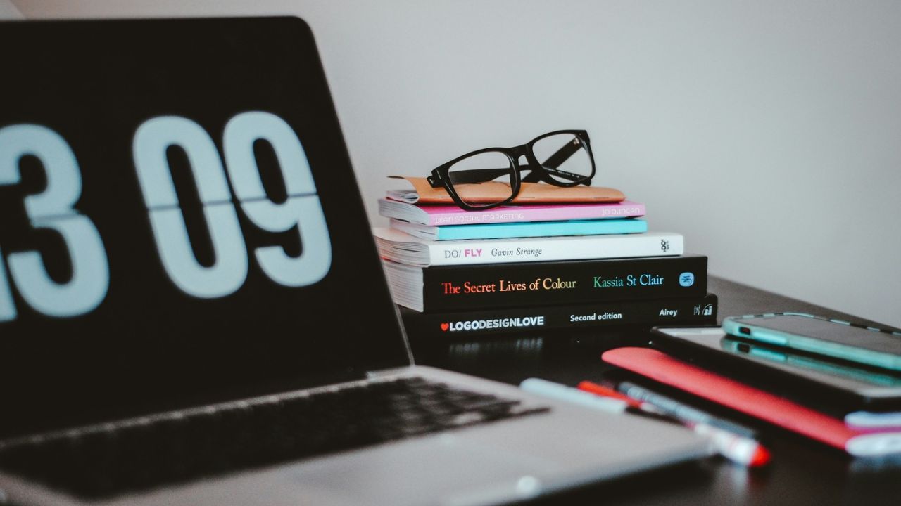 computer laptop next to books, pens and glasses indoors on desk