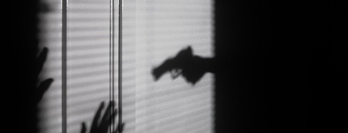 shadow on blinds of a person holding a gun towards a victim