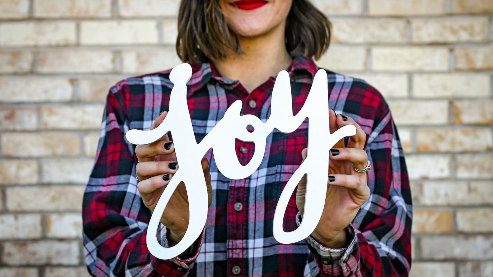 A picture of a woman, outside, holding a joy sign