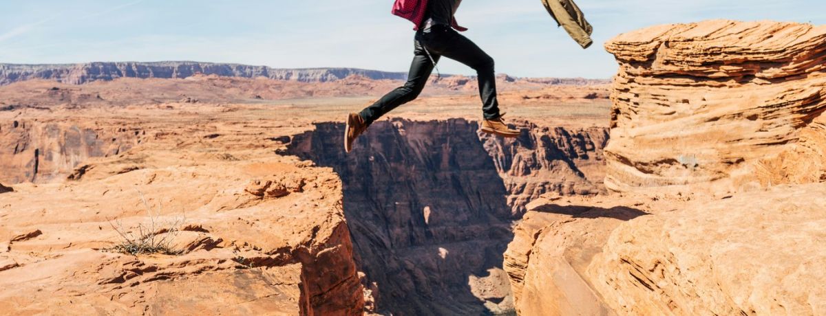 guy jumping over a chasm outdoors in desert