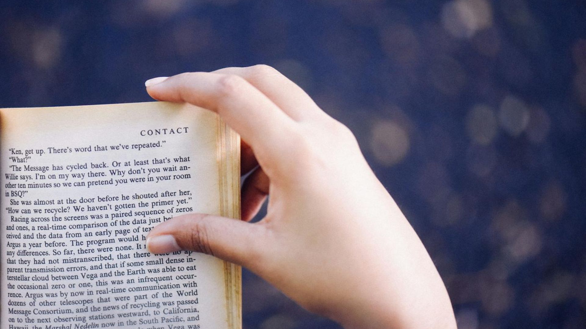 person reading a book indoors, with hand on book