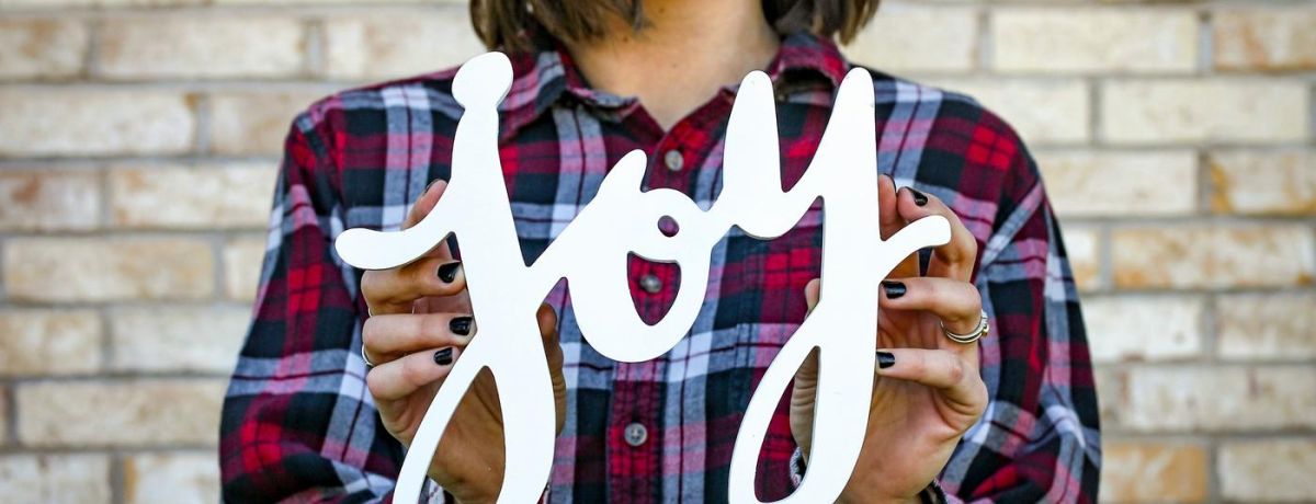 A picture of a woman, outside, holding a joy sign