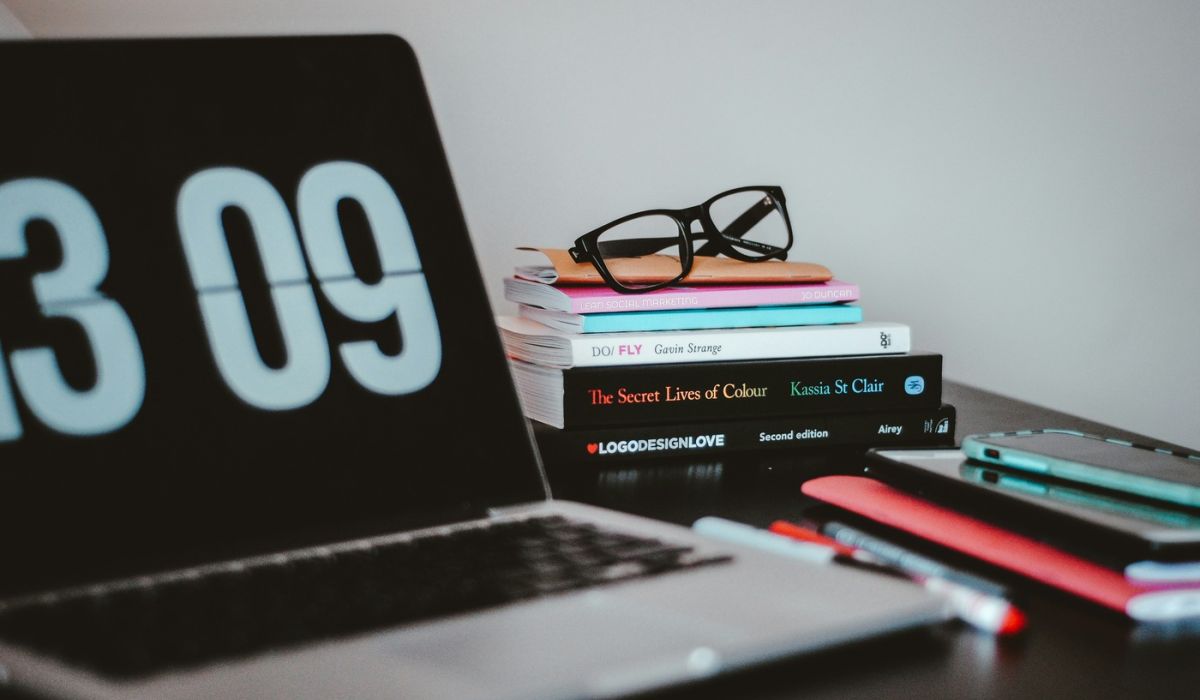 computer laptop next to books, pens and glasses indoors on desk