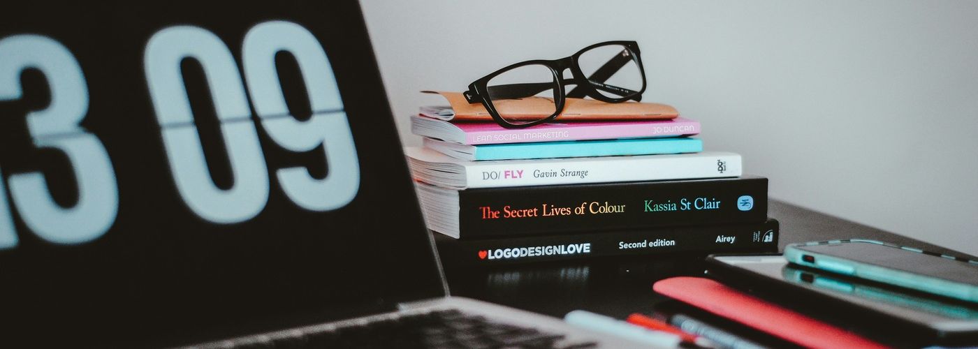 computer laptop next to books, pens and glasses indoors on desk