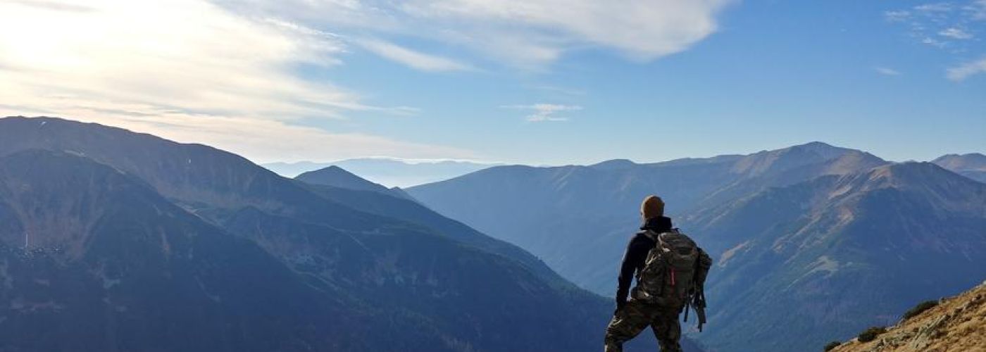 adventure: man standing on the edge of a cliff looking out at the mountains