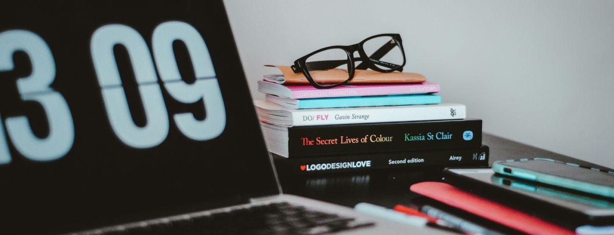 computer laptop next to books, pens and glasses indoors on desk