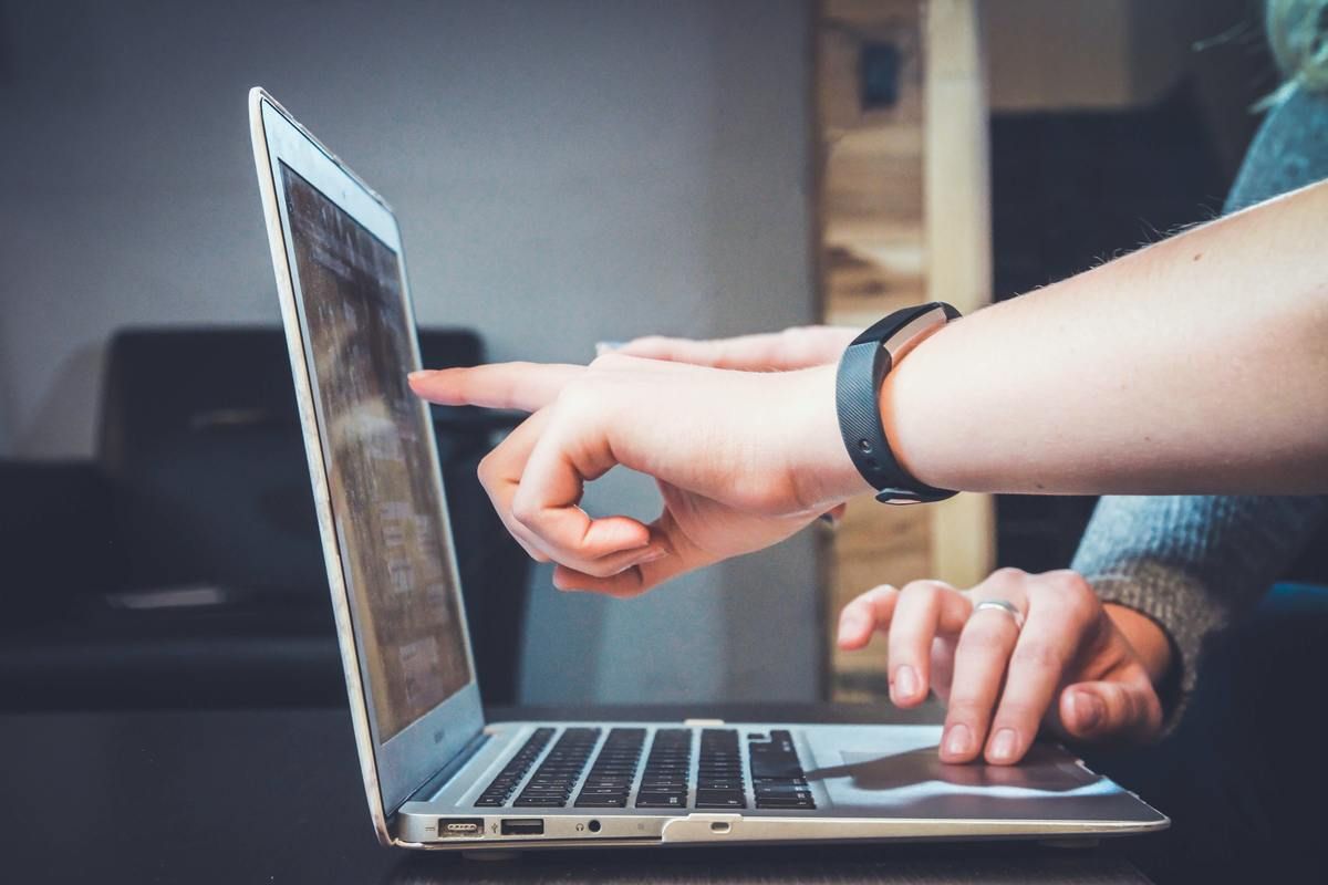 two people working together indoors at a desk pointing at a computer