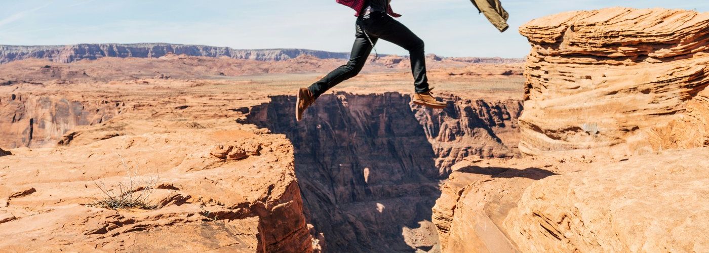 guy jumping over a chasm outdoors in desert